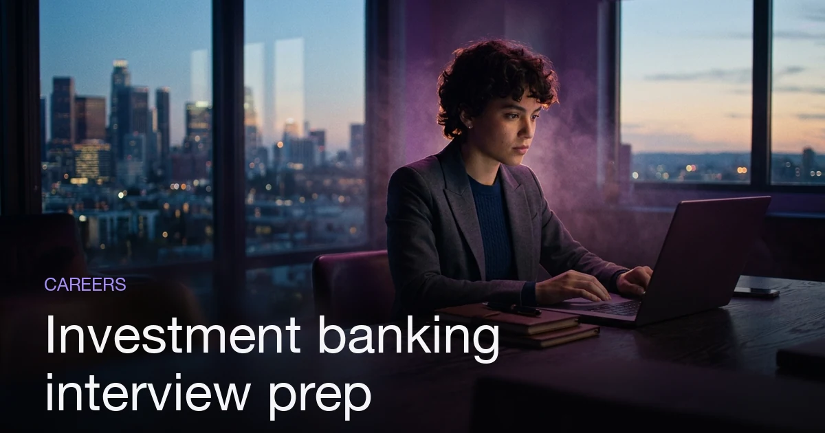 A finance student doing investment banking interview preparation at a desk with a financial-district skyline at dusk.