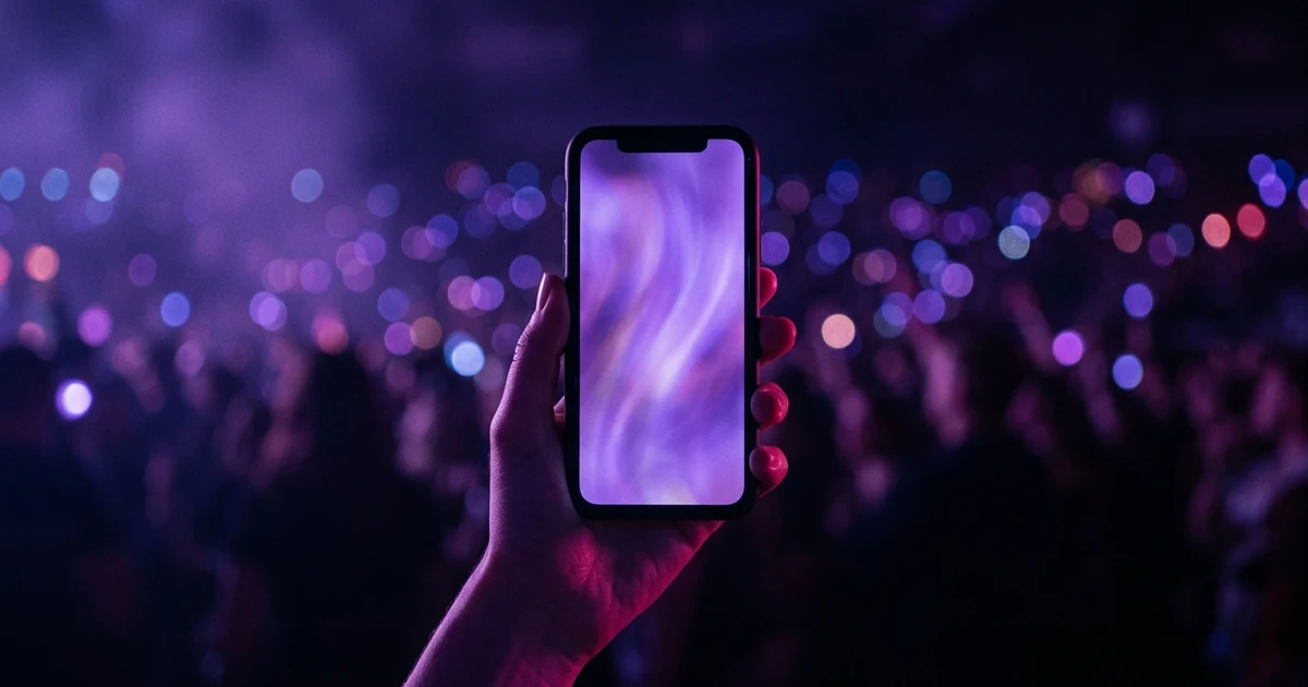 A hand holding a phone whose display shows a soft looping vertical violet visual, with bokeh lights behind in the dark.